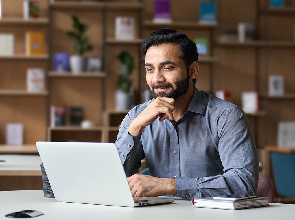 smiling,indian,businessman,working,on,laptop,in,modern,office,lobby